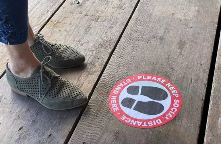 Foto de zapatos de una persona delante de Vinilo Antideslizante en forma de circulo con aviso de precaución en un suelo de madera